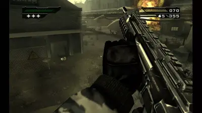 First-person view holding an assault rifle in a dusty industrial yard in BLACK, a fire burning behind a building ahead